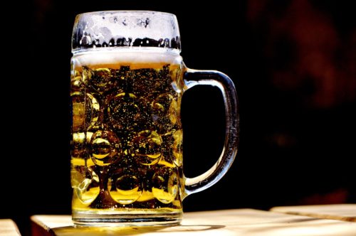 A large glass beer mug filled with light, bubbly beer sits on a wooden surface against a dark background. As condensation forms on the intricately designed glass, it's a sobering reminder of the potential damages caused by drunk drivers if they don't drink responsibly.