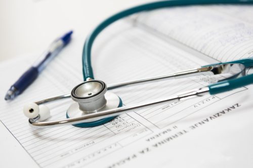 A stethoscope rests on a medical chart with text, next to a blue pen, as a specialist makes crucial notes. The page appears to contain patient information and recommendations, suggesting a healthcare or medical setting.