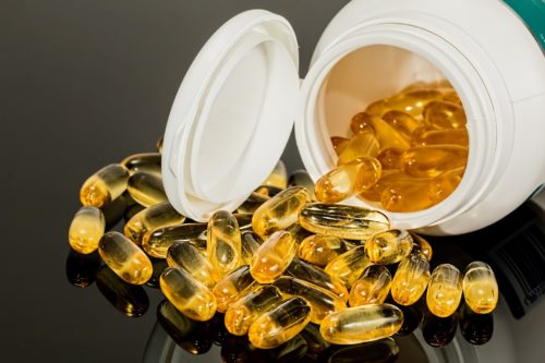 A white plastic bottle tipped over on a glossy surface in Washington D.C., spilling numerous yellow gel capsules. The shiny, translucent capsules suggest a potential medication error, indicating they might be a dietary supplement or vitamin.