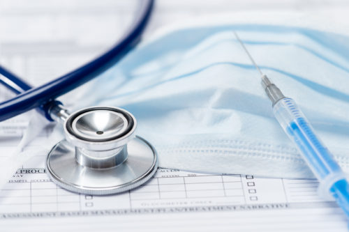 A stethoscope, a disposable face mask, and a syringe lie on a paper form. The blue tubing matches the mask's color, while the syringe is filled with a clear liquid. This scene subtly hints at medical negligence concerns within healthcare settings.